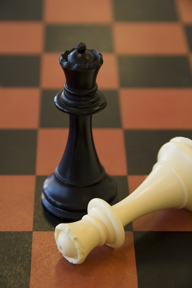 Black queen stands victorious over fallen white queen on chessboard